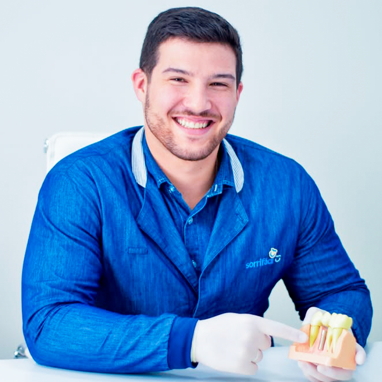Dr. Matheus sorrindo e apresentando um modelo de implante dentário